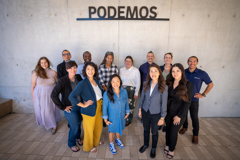 Thirteen Eighth College Staff Members Smiling Underneath Building with Podemos Sign Above